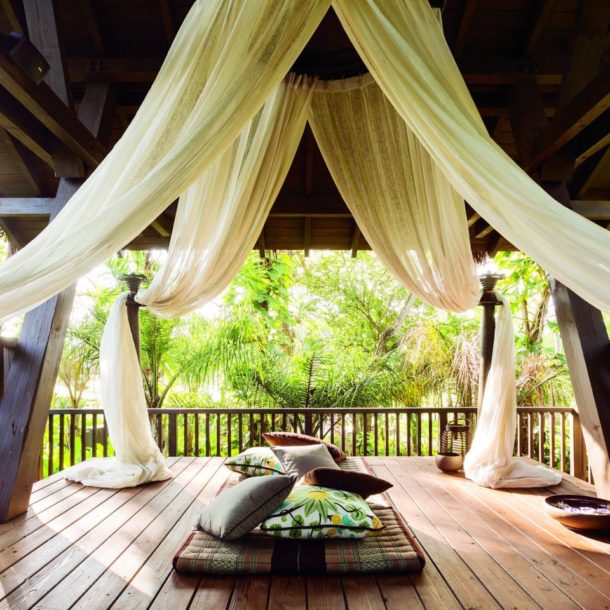 Balcony with drapes and pillows surrounded by tropical plants at resort.