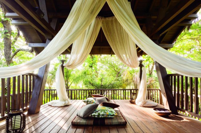 Balcony with drapes and pillows surrounded by tropical plants at resort.
