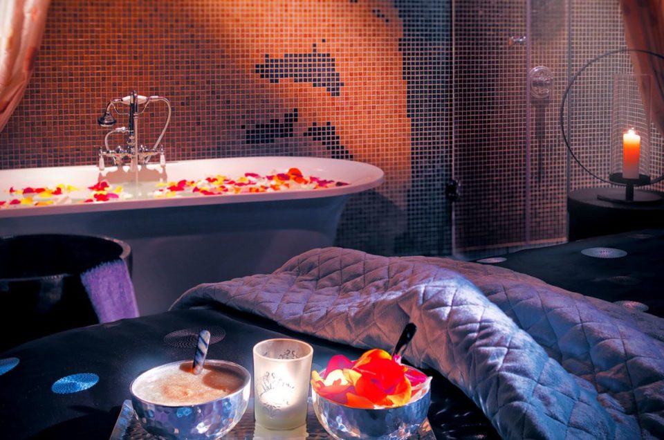 Massage bed and bath with candles on flower petals.