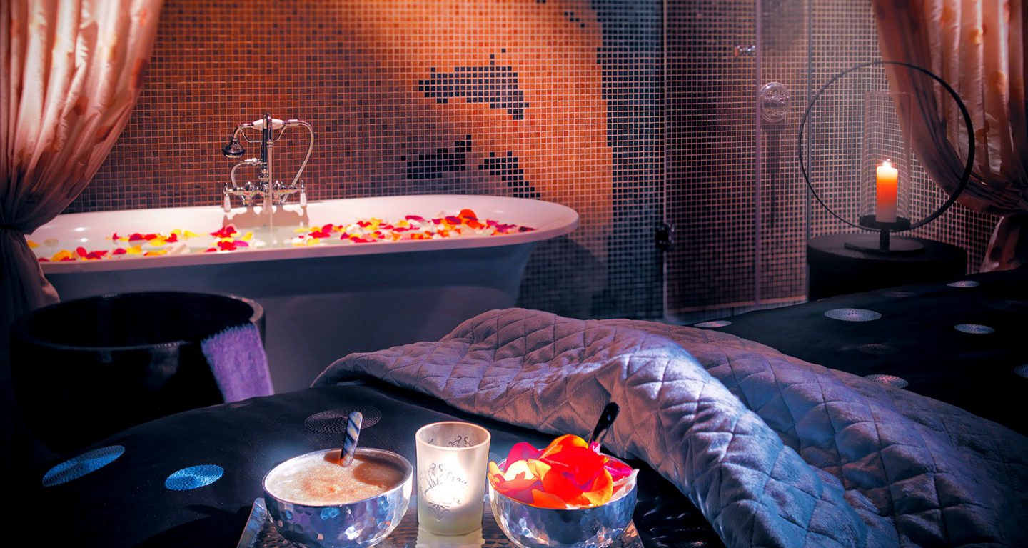Massage bed and bath with candles on flower petals.