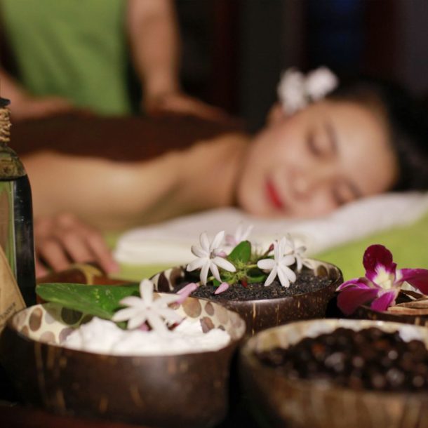 Woman receiving massage in background while essential oils and aromatics are shown in foreground.