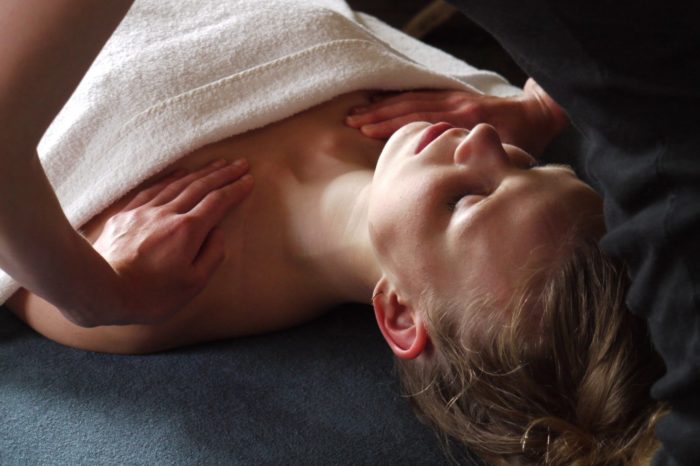 Woman in towel on massage bed getting a shoulder massage while eyes closed.